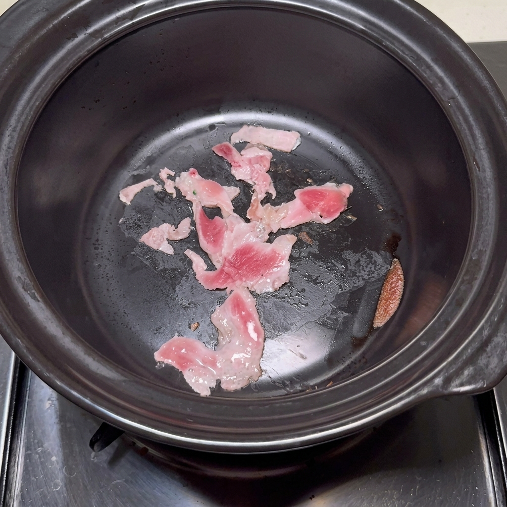 Agua clara siendo vertida con un cucharón en una olla de piedra que contiene la panceta sellada.