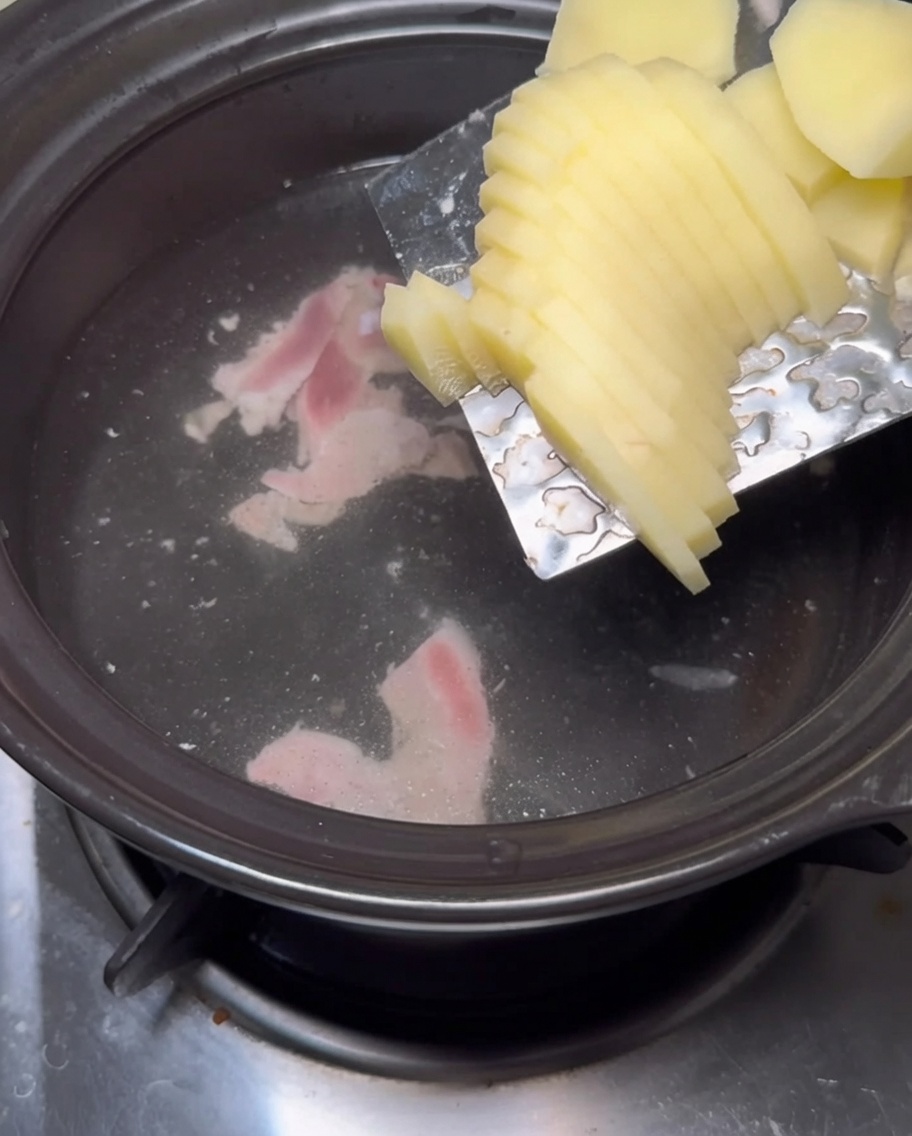 Rodajas gruesas de patata deslizándose desde una hoja de metal hacia una olla de agua hirviendo.