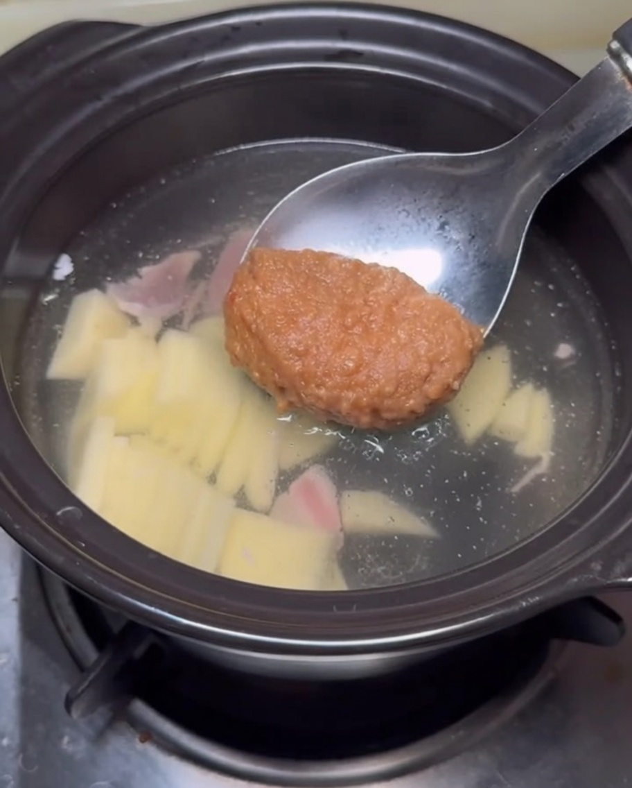 Un cucharón con una porción de pasta de soja espesa siendo sumergido en el caldo del estofado.