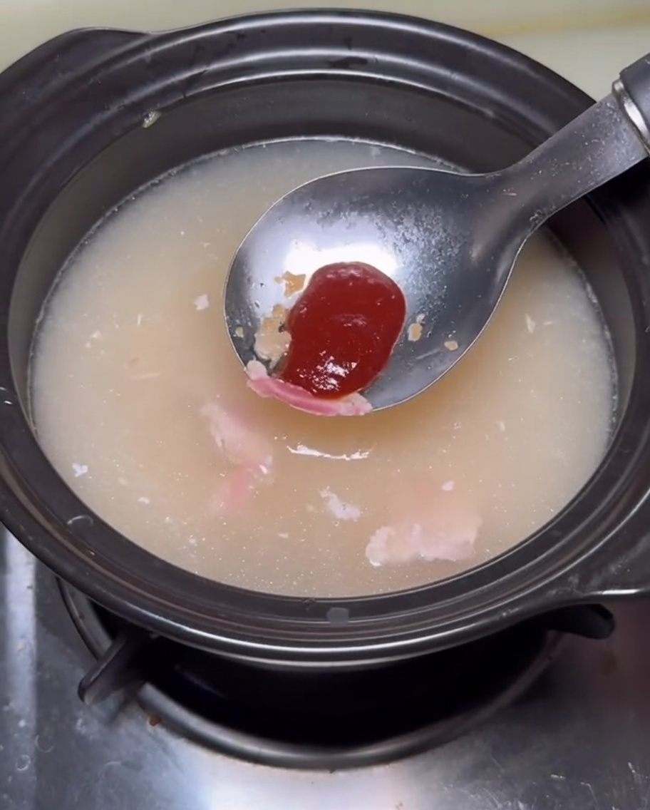 Una cucharada de salsa rojiza siendo añadida a la olla de caldo.