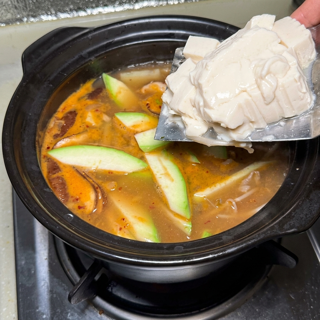Bloques de tofu sedoso deslizándose desde un cuchillo al estofado burbujeante.