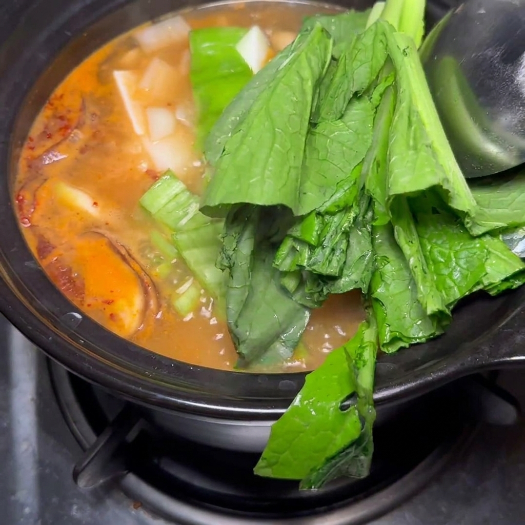 Baby bok choy fresco y trozos de cebolla siendo añadidos al estofado finalizado.