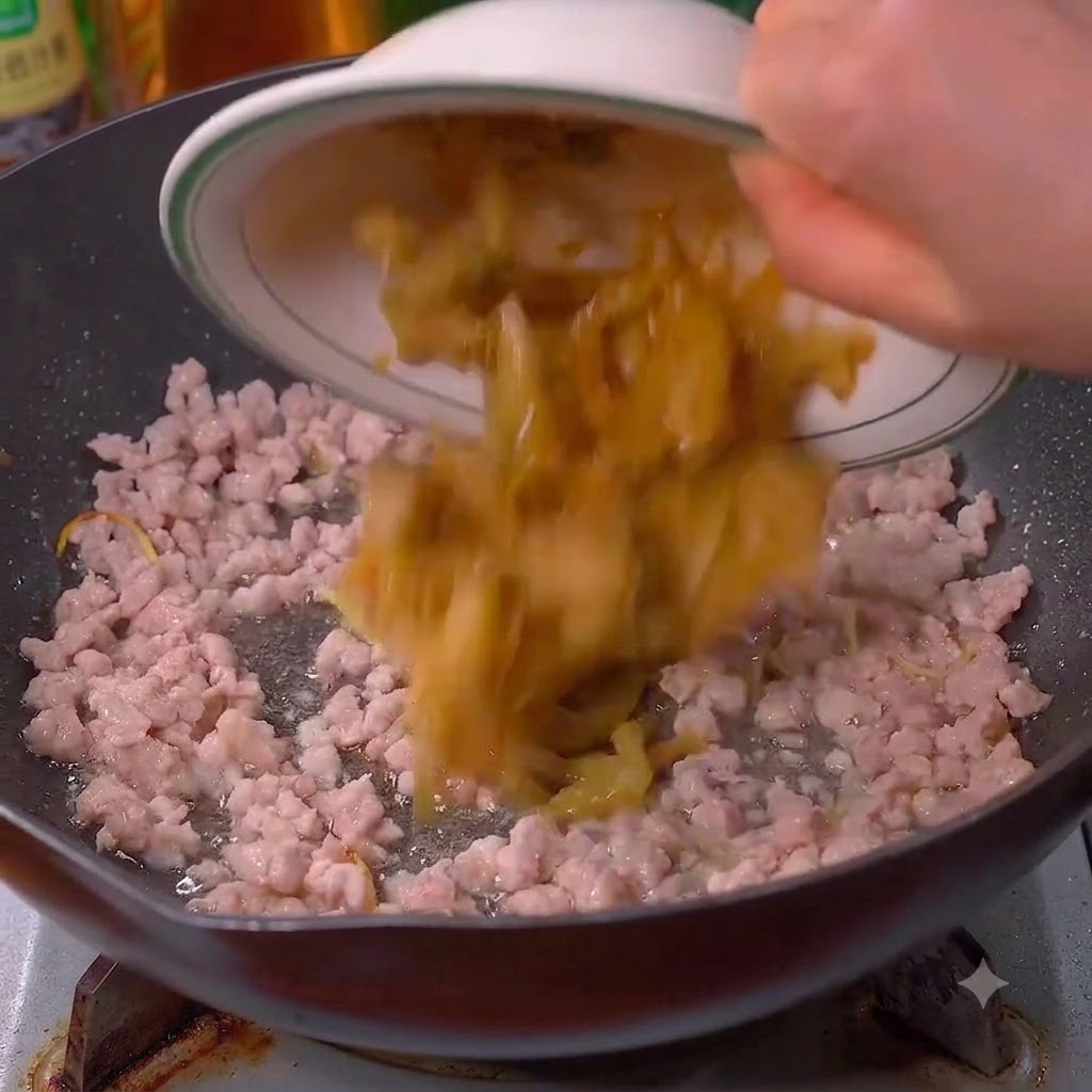 Verduras de mostaza encurtidas siendo vertidas en el wok con el cerdo.