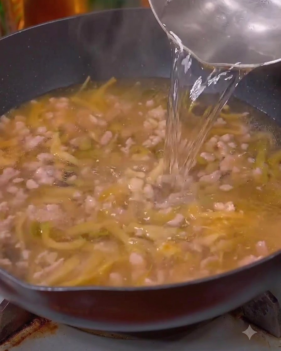 Agua siendo vertida en el wok sobre la carne y las verduras.