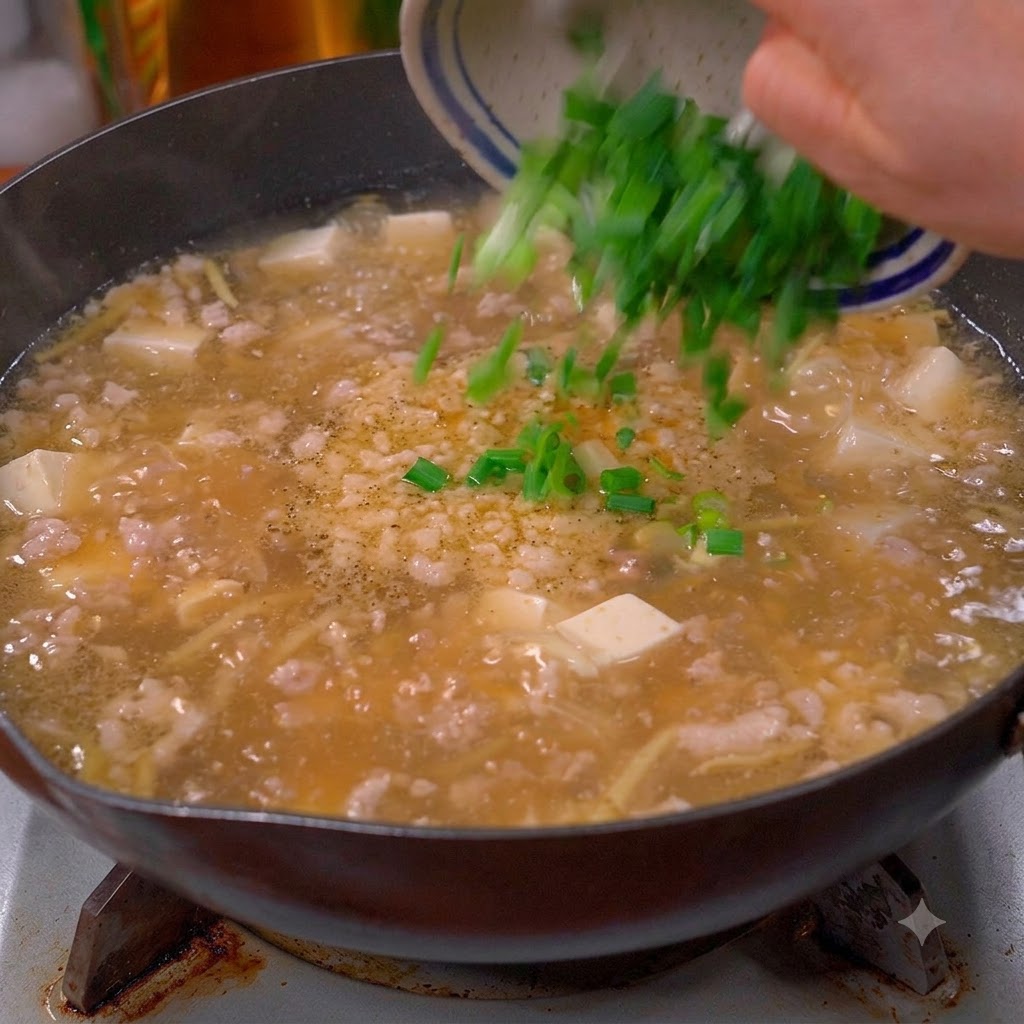 Cebollinos verdes picados y cilantro siendo vaciados desde un bol hacia una olla de sopa burbujeante.