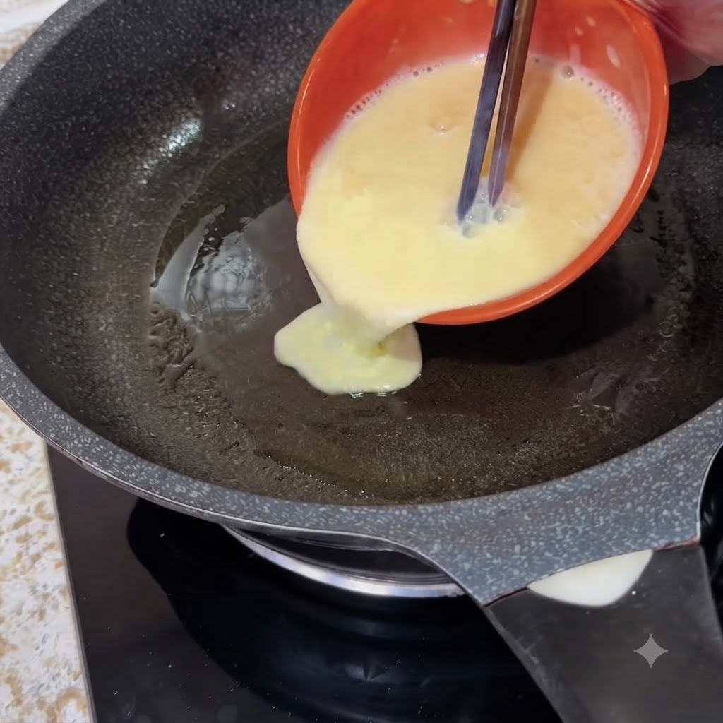 Un bol naranja vertiendo huevos batidos líquidos con palillos en una sartén caliente.