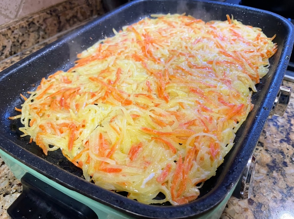 Una gran tortilla de patata siendo cortada en porciones más pequeñas con espátulas de cocina en una sartén.