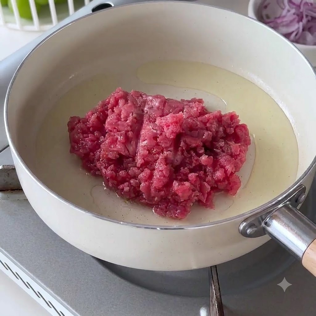 Carne picada cruda colocada en una sartén blanca caliente con aceite.