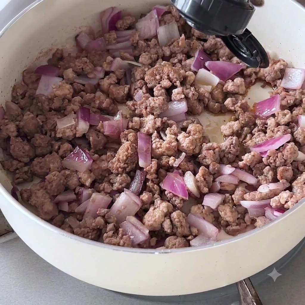 Salsa oscura vertiéndose desde una botella sobre la carne picada y la cebolla cocinada en una sartén.