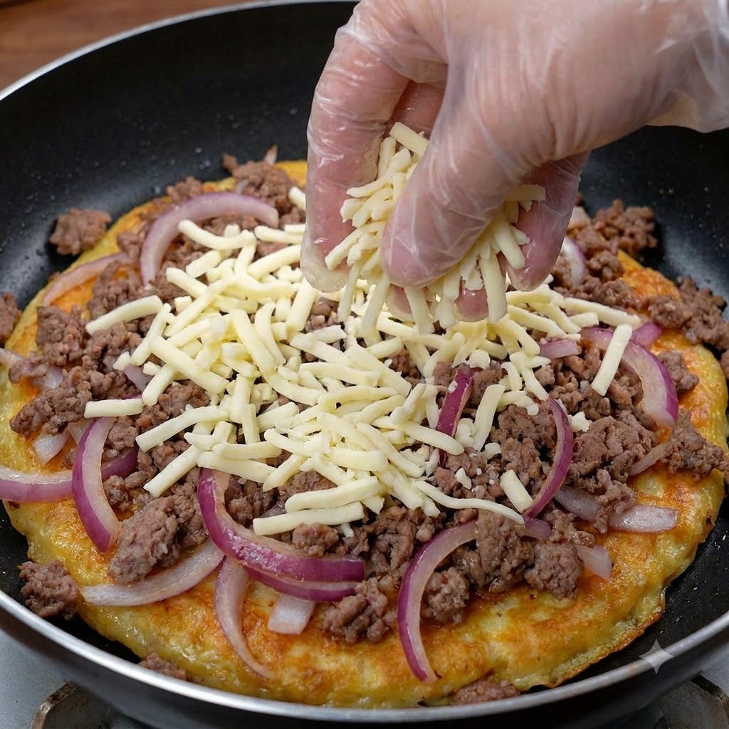 Una mano con guante espolvoreando una gruesa capa de queso rallado sobre una mezcla de carne y cebolla en una sartén.