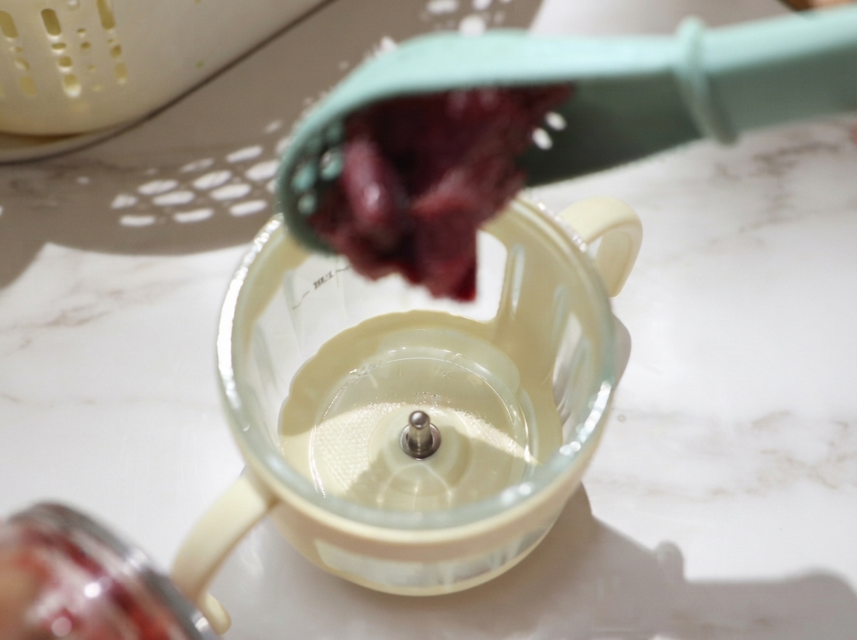 Trozos escurridos de ternera cruda siendo colocados en el vaso de un pequeño procesador de alimentos para triturar.