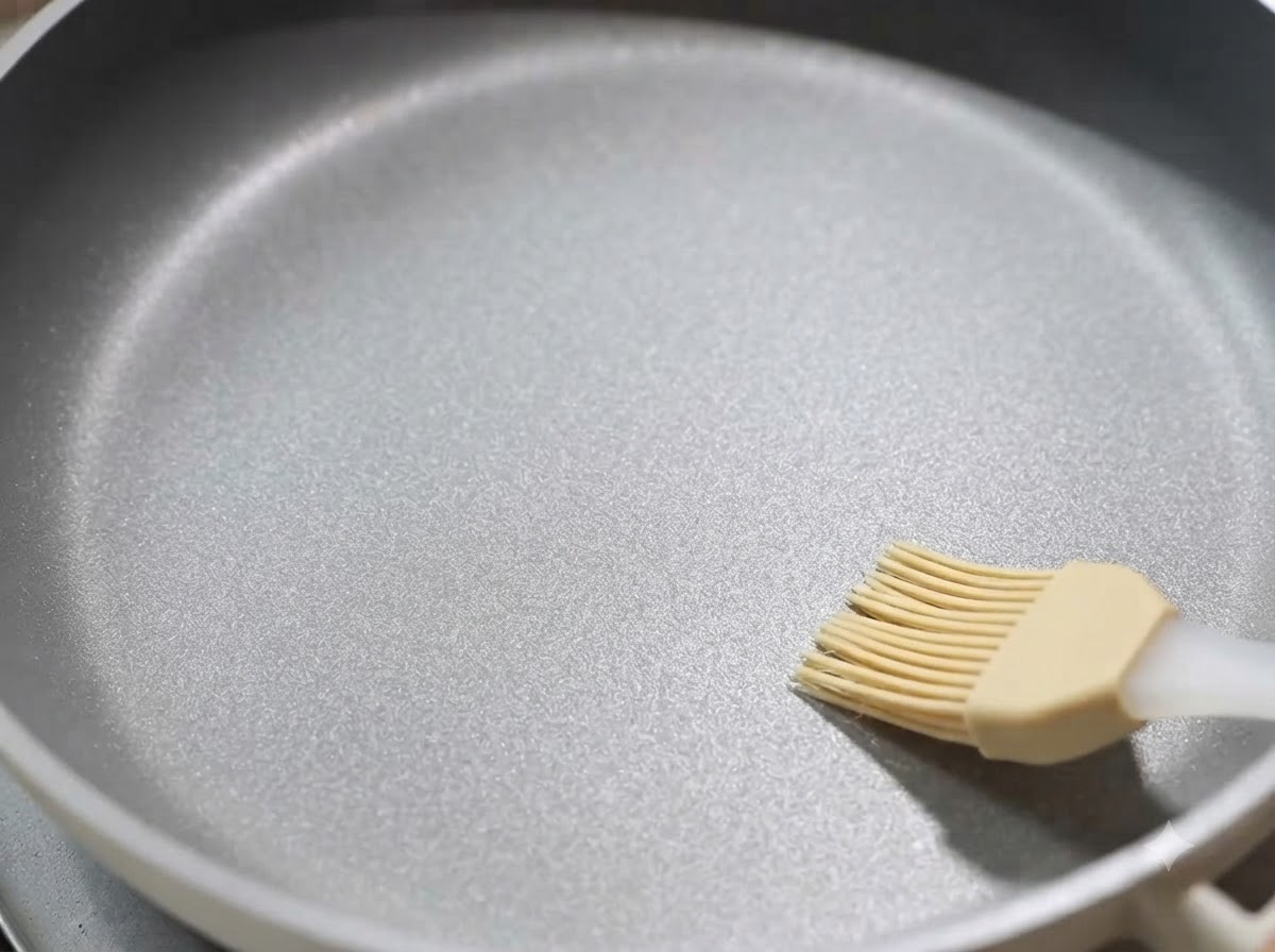Una sartén antiadherente siendo pincelada con una capa fina de aceite de cocina.