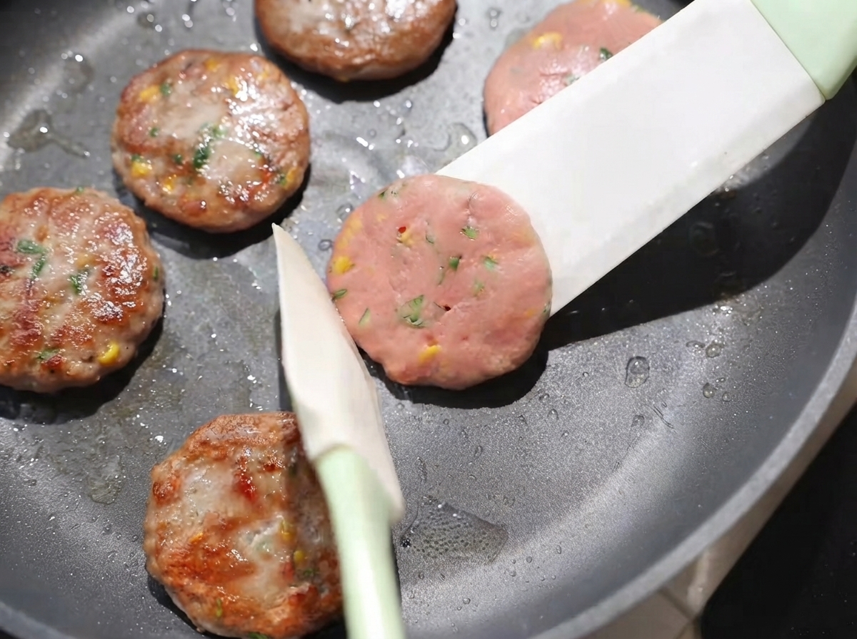Albóndigas siendo volteadas en la sartén con una espátula, mostrando superficies doradas cocinándose a fuego lento.