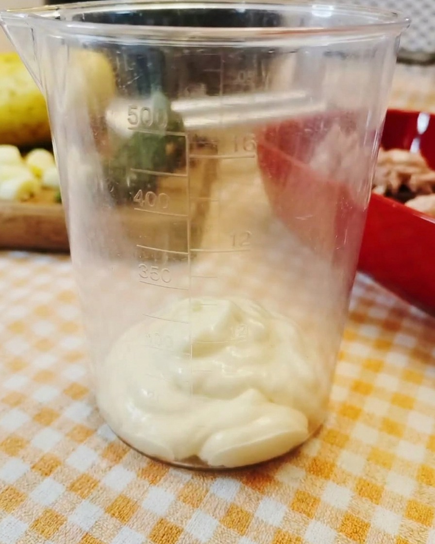 Una cucharada de mayonesa espesa reposando en el fondo de un vaso medidor de plástico transparente.