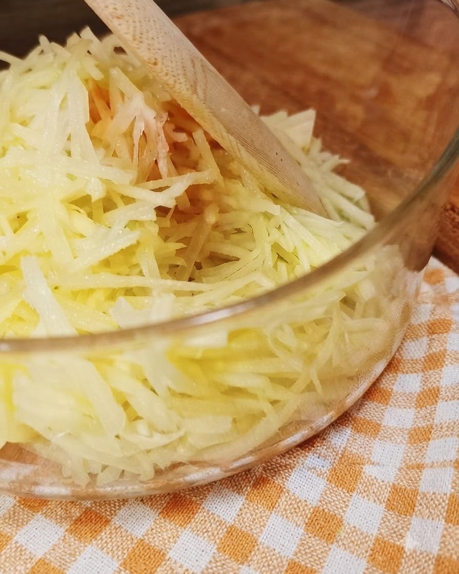 Patatas recién ralladas dentro de un tazón de vidrio transparente con un utensilio de madera.