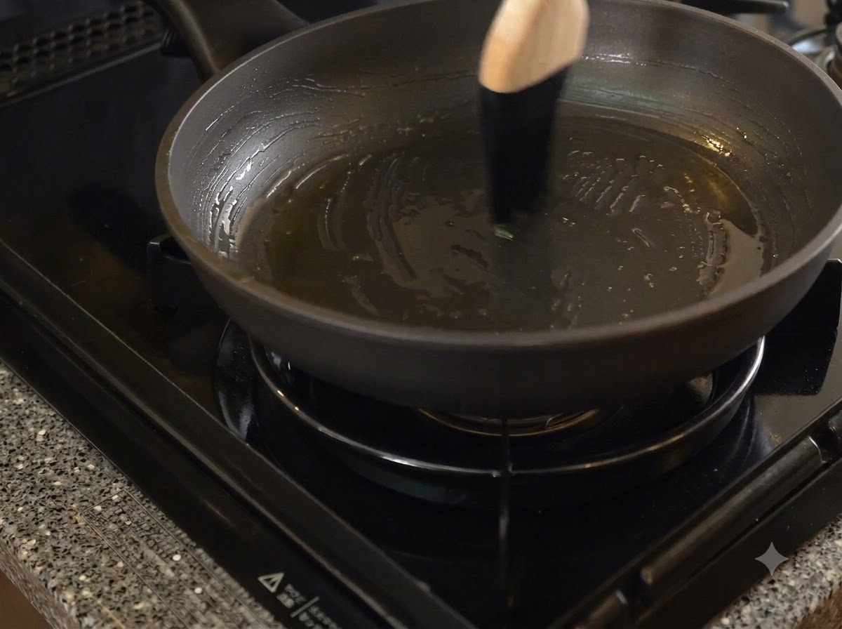 Una sartén antiadherente oscura siendo untada con manteca de cerdo usando una brocha de cocina con mango de madera.