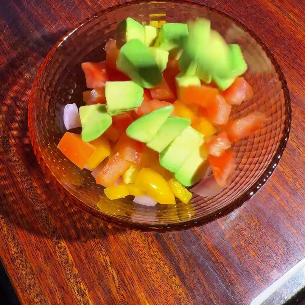 Vegetales picados y aguacate en un tazón de vidrio mezclándose con el aliño.