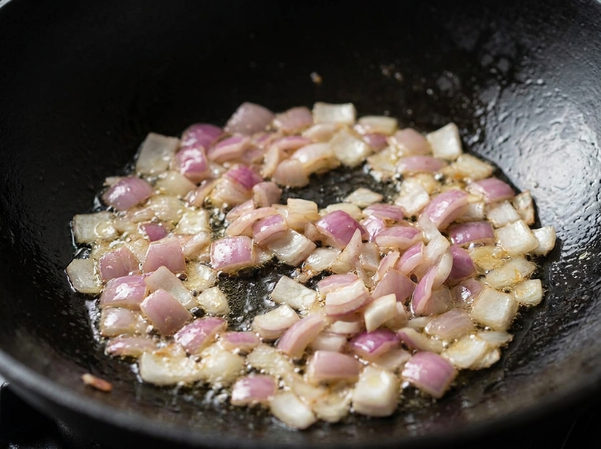 Cebollas rojas picadas y tocino cociéndose y chisporroteando en aceite dentro de un wok negro.