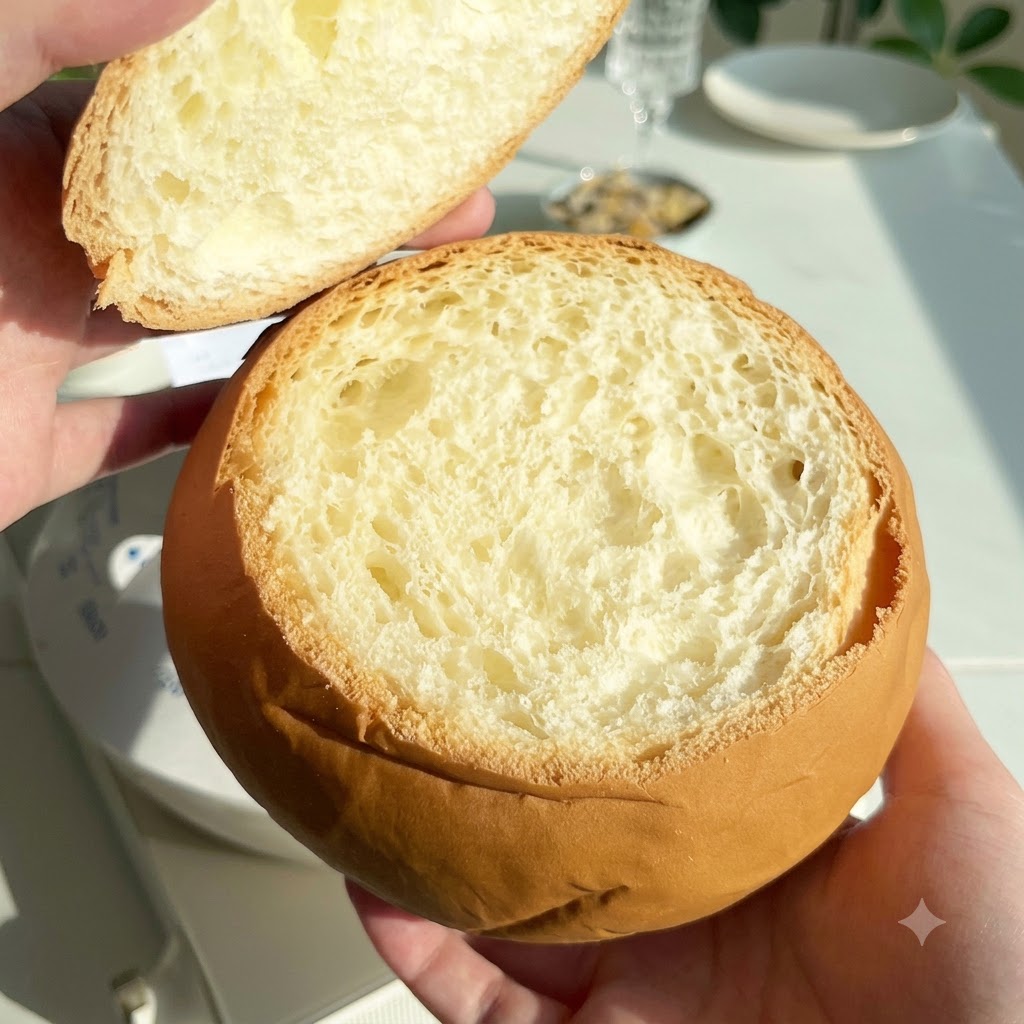 Una hogaza de pan redonda y ahuecada sostenida con su tapa superior retirada a un lado.