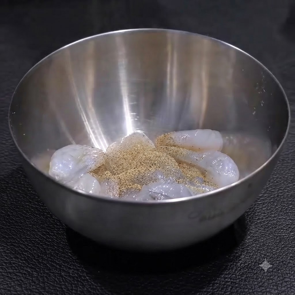 Camarones crudos dentro de un tazón de acero inoxidable sazonados con una capa de pimienta y sal, listos para ser mezclados.