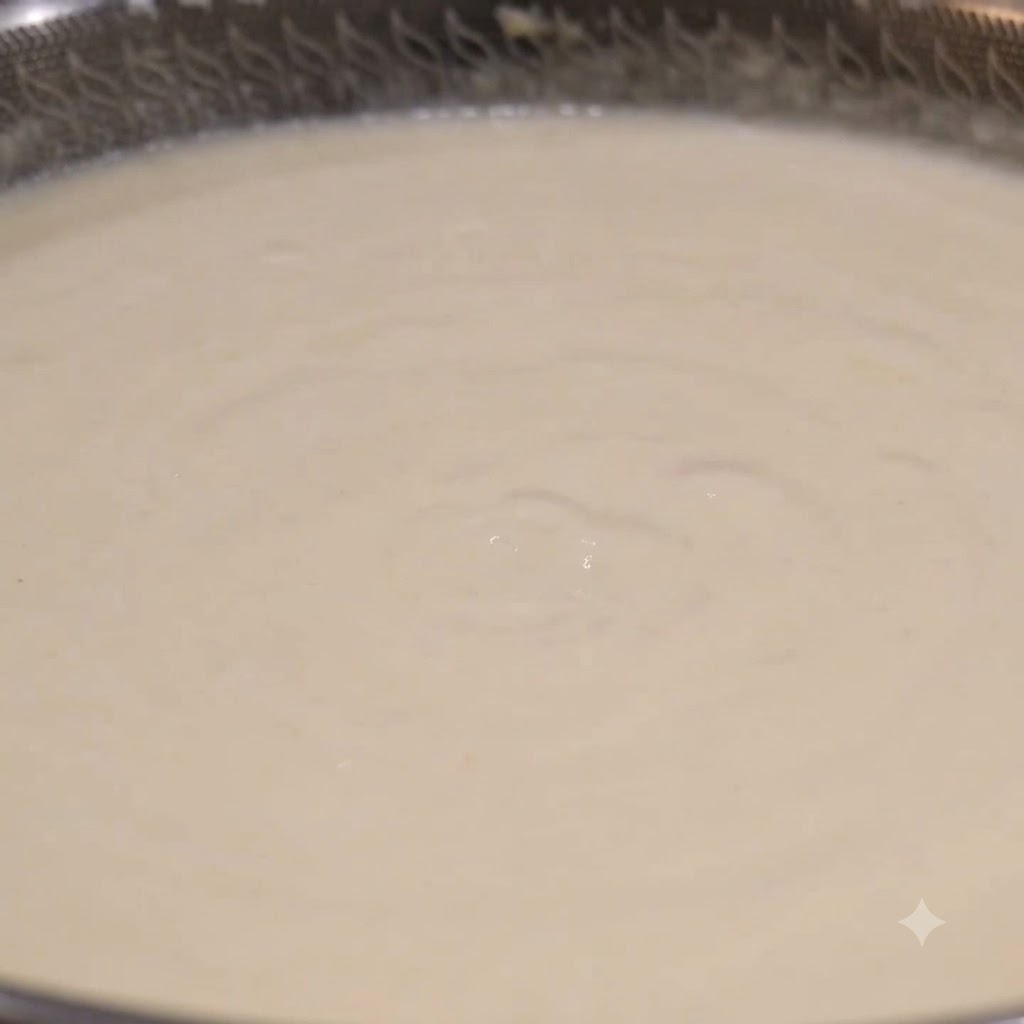 Un cucharón tomando sopa de almejas blanca y cremosa de un wok a fuego lento.