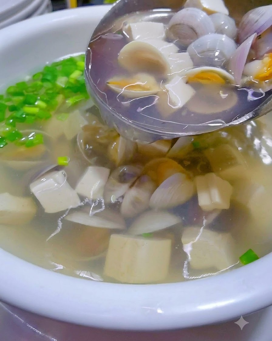 Sopa caliente de almejas y tofu siendo vertida desde un wok en un tazón de servicio adornado.