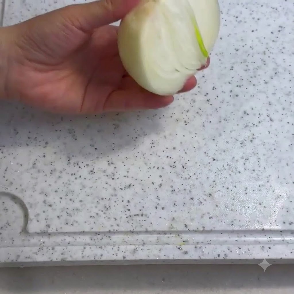 Una cebolla siendo cortada en una tabla de cortar blanca con un cuchillo.