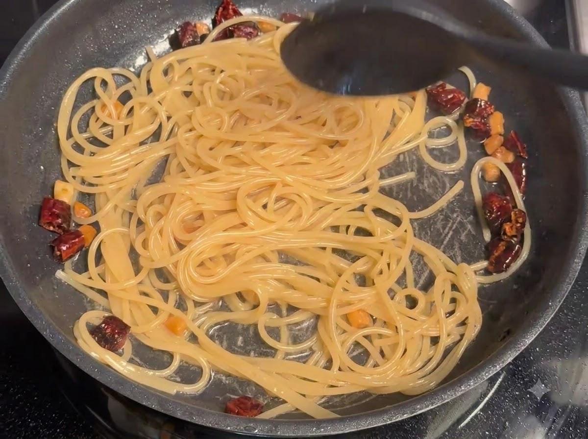 Agua de la pasta siendo revuelta con los espaguetis y el cerdo en una sartén.