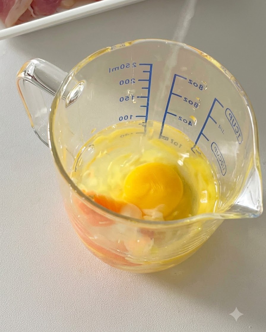 Huevos, queso parmesano rallado y pimienta negra combinados dentro de una taza medidora de cristal.