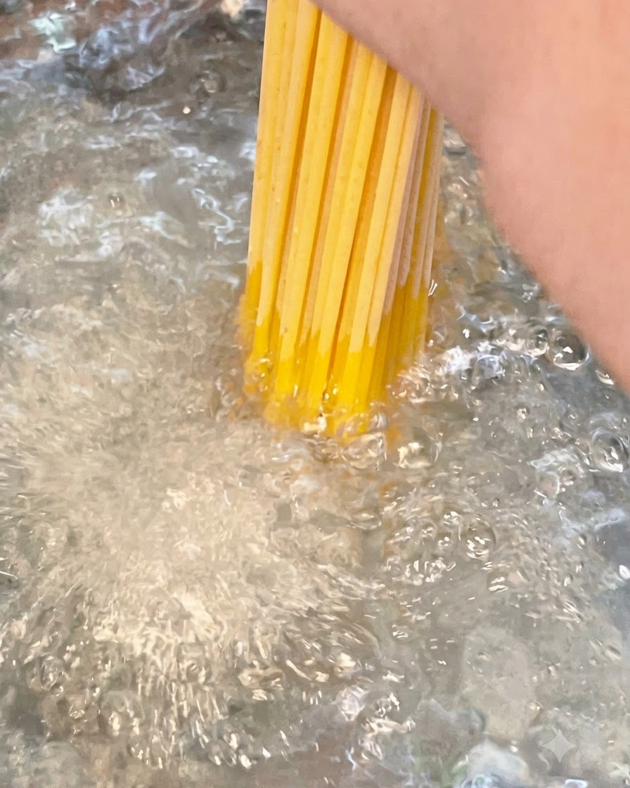 Un paquete de fideos largos de espagueti secos sumergiéndose en una olla con agua hirviendo con sal.