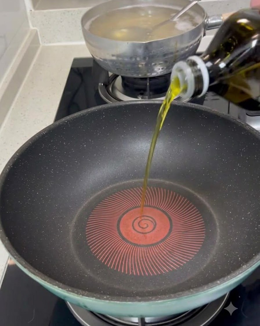 Aceite de oliva virgen extra siendo vertido desde una botella en el centro de una sartén oscura precalentada.