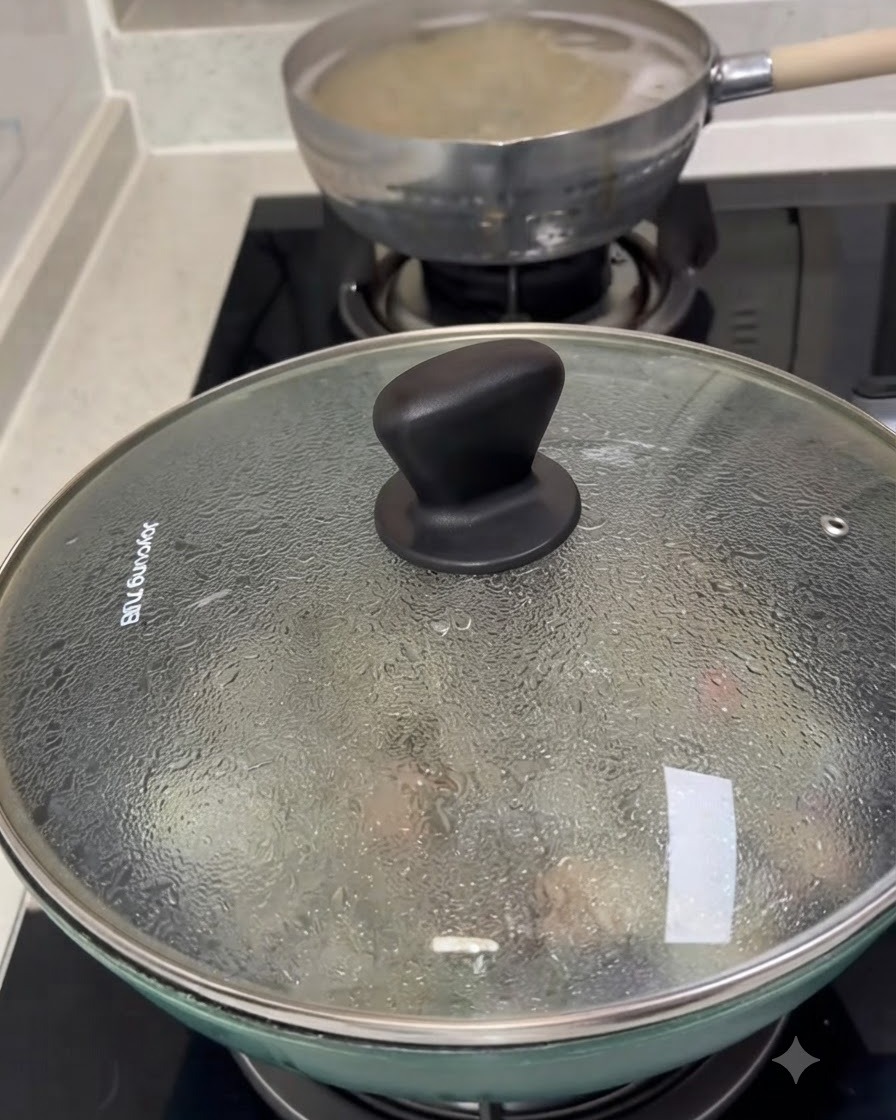 Una tapa de vidrio cubriendo una sartén llena de almejas cocinándose, con condensación visible en la superficie.