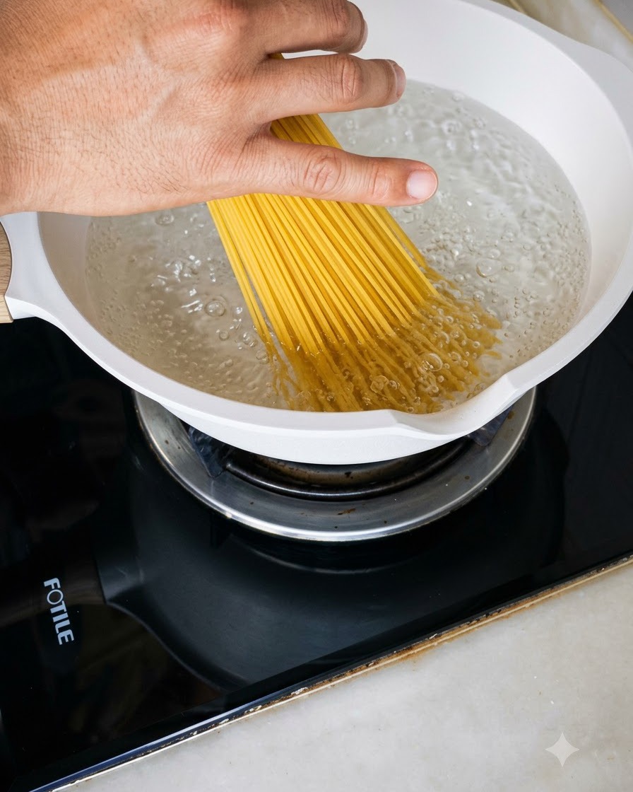 Un puñado de espaguetis secos introduciéndose en una olla blanca llena de agua hirviendo burbujeante.
