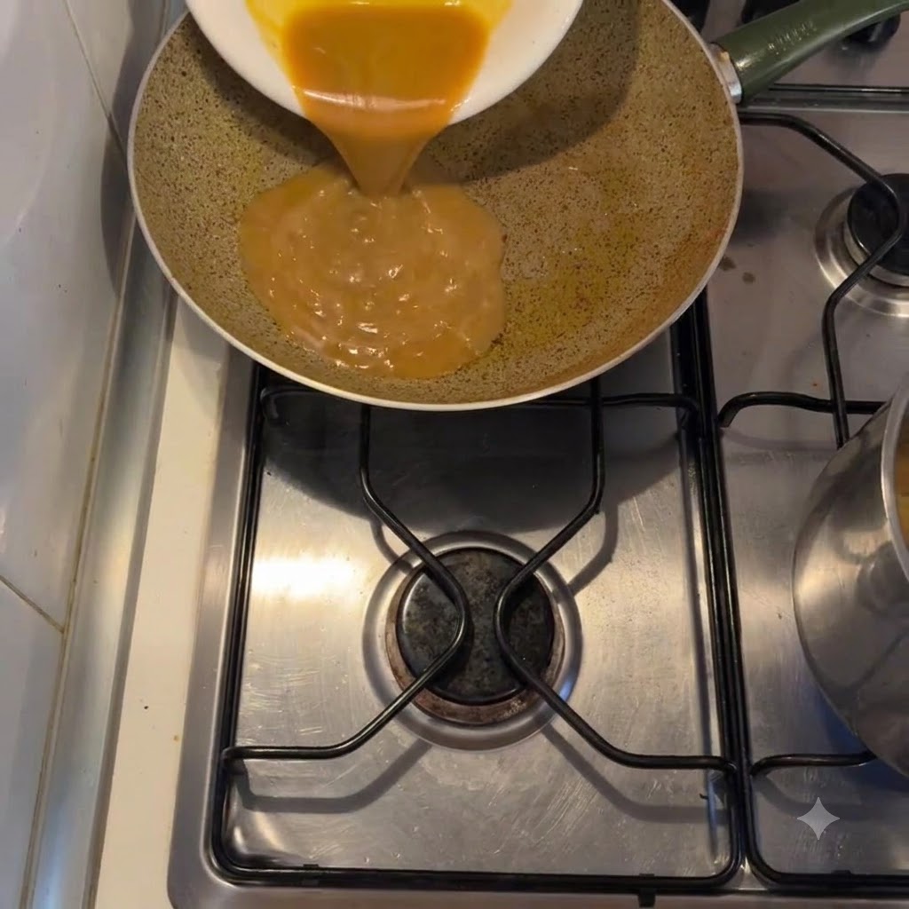 Salsa dorada y espesa vertiéndose desde un plato blanco a una sartén al fuego.