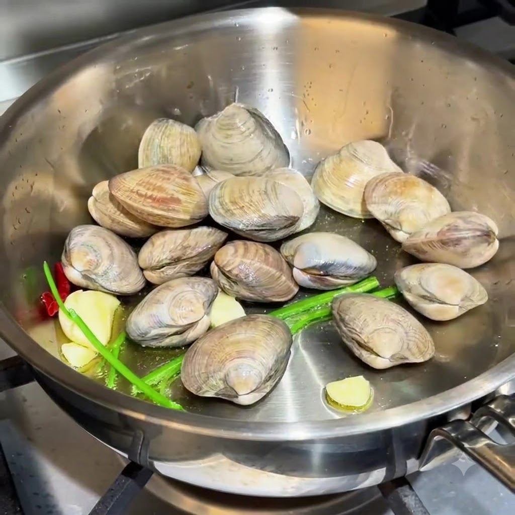 Almejas esparcidas en la sartén junto con el ajo y las raíces de cebollino.