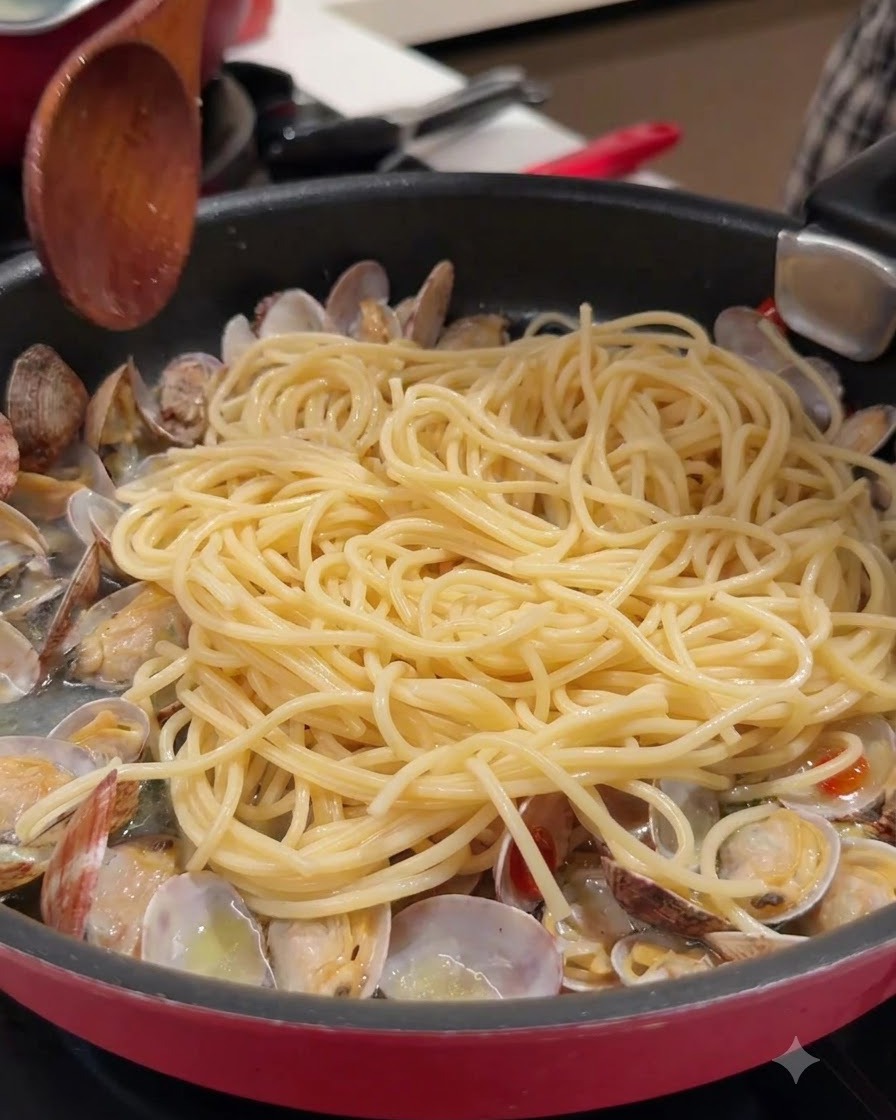 Una cuchara de madera y pasta de espagueti en una sartén con almejas abiertas y caldo.
