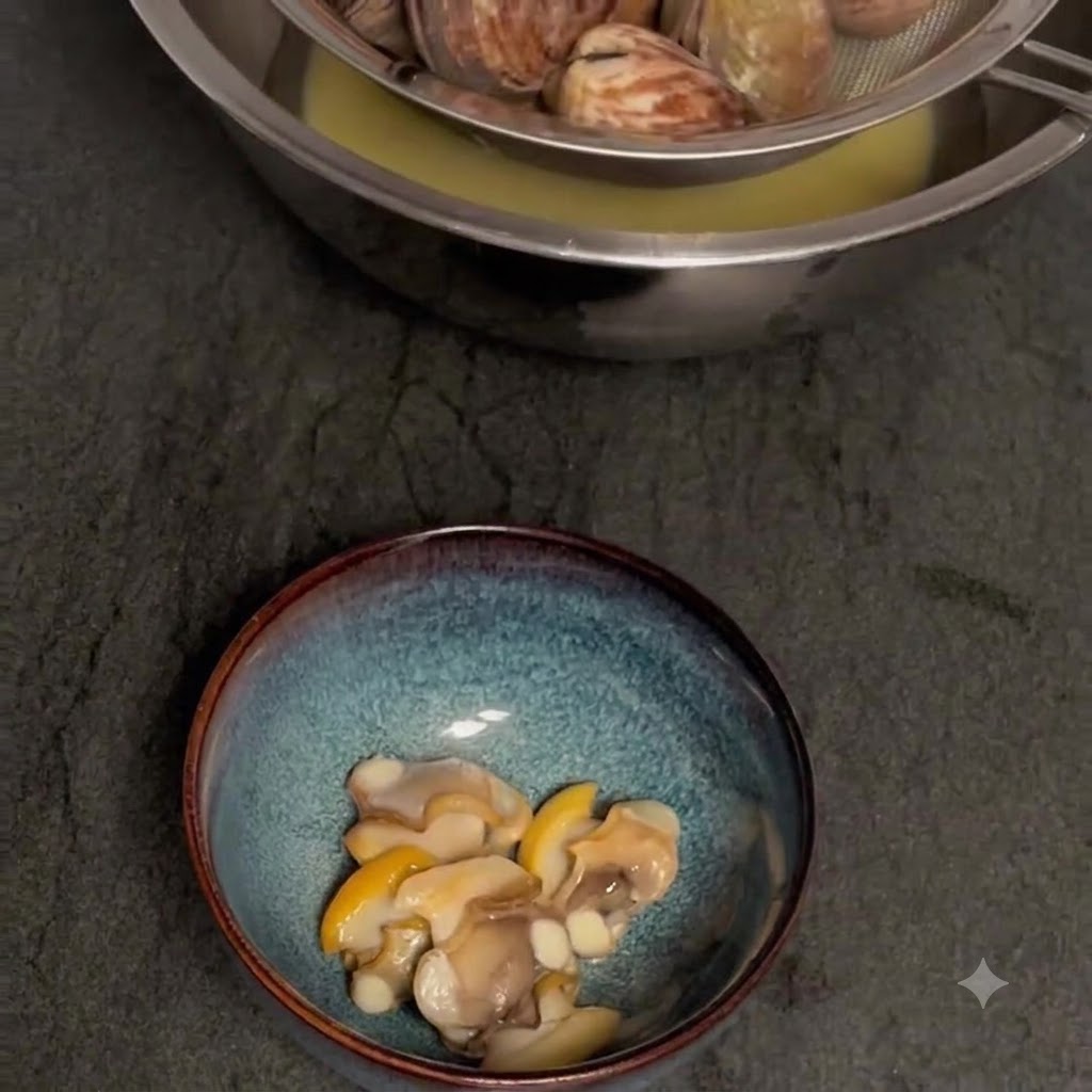 Almejas cocidas coladas sobre un bol para recoger el caldo, con la carne de almeja sin cáscara en un bol separado debajo.