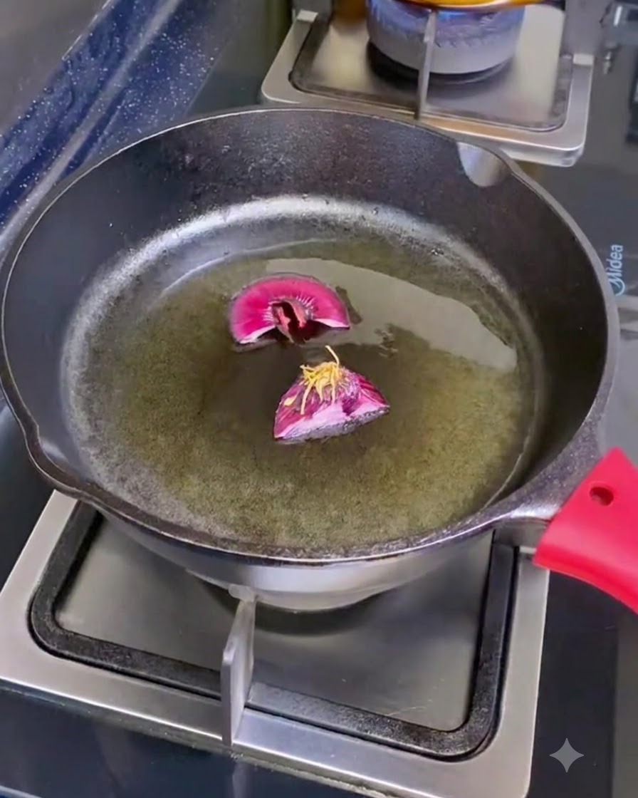 Una sartén de hierro fundido en un quemador que contiene aceite de oliva y dos trozos cortados de raíces de chalota.
