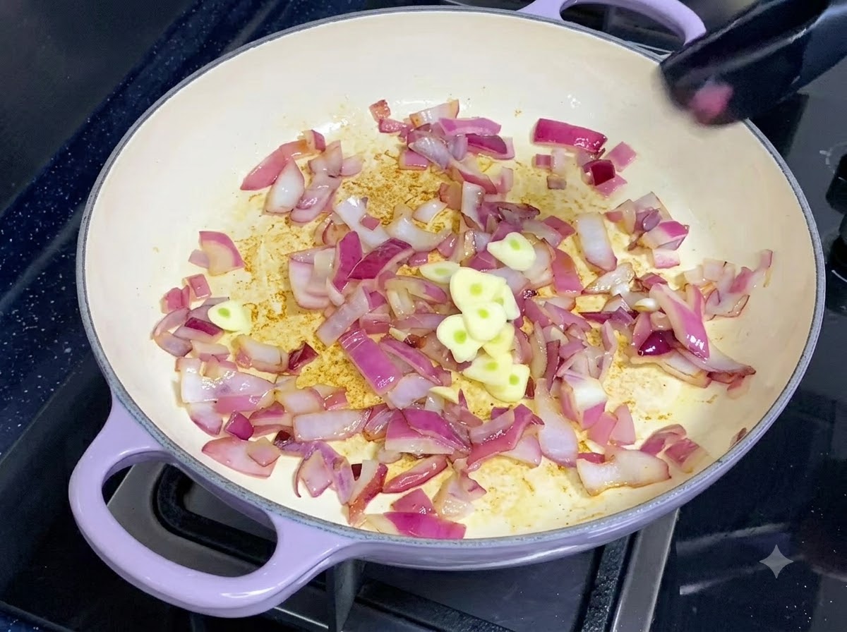 Rodajas de ajo fresco siendo añadidas a una sartén con cebollas rojas sofritas.