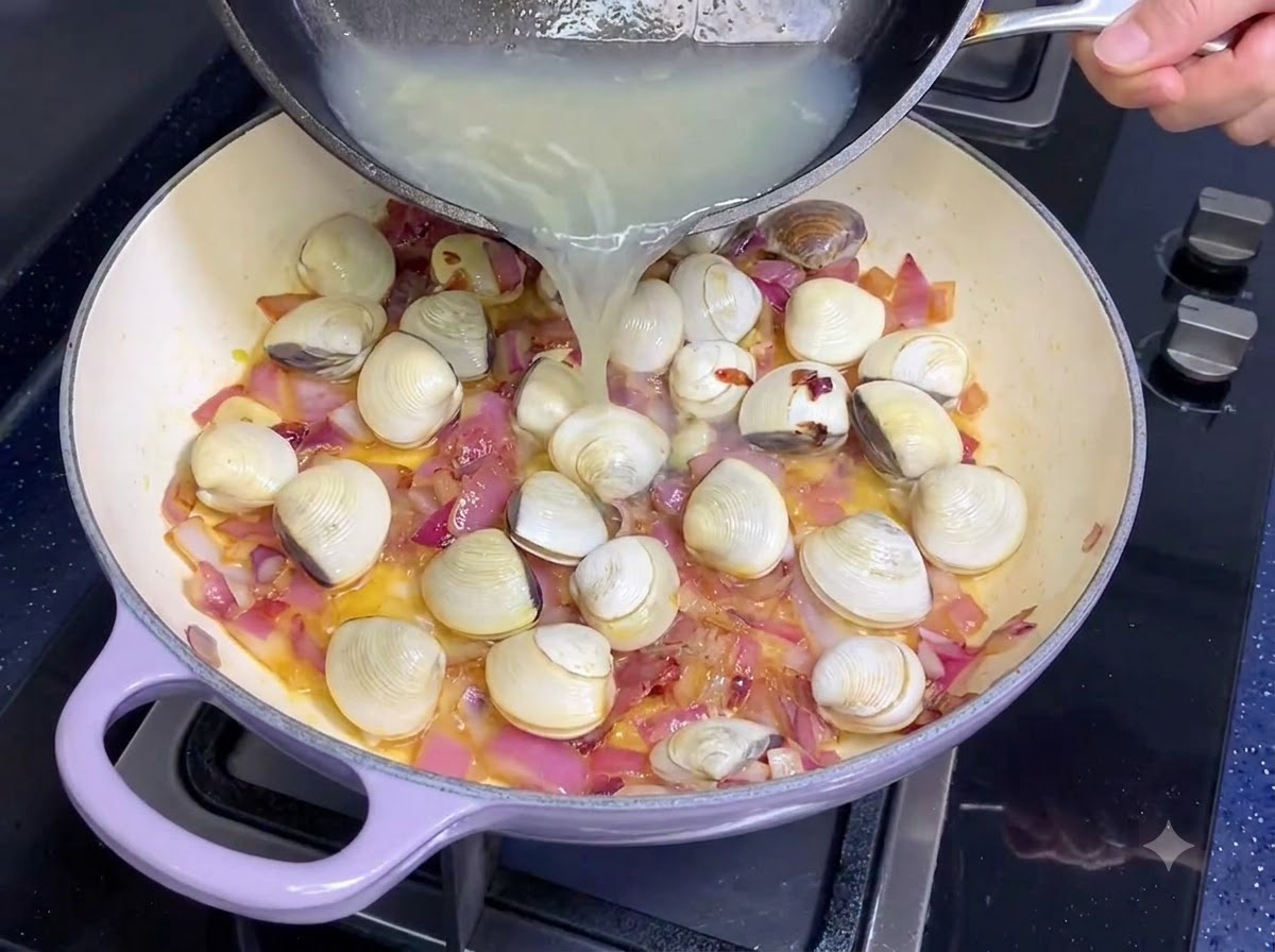 Caldo de almejas siendo vertido desde una sartén a otra con cebollas y ajo.