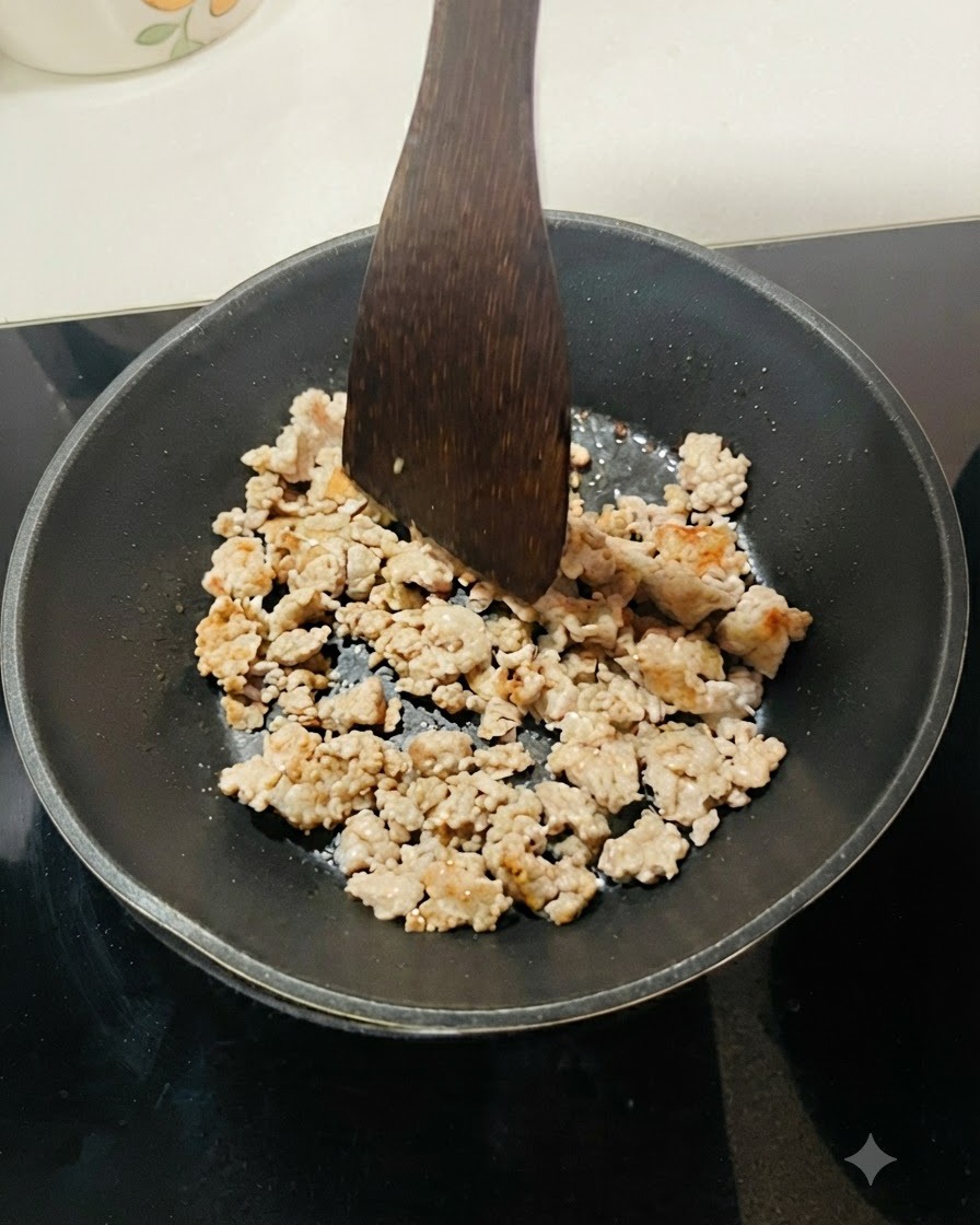 Carne picada dorándose en una sartén negra, separada en pequeños trozos con una espátula de madera.