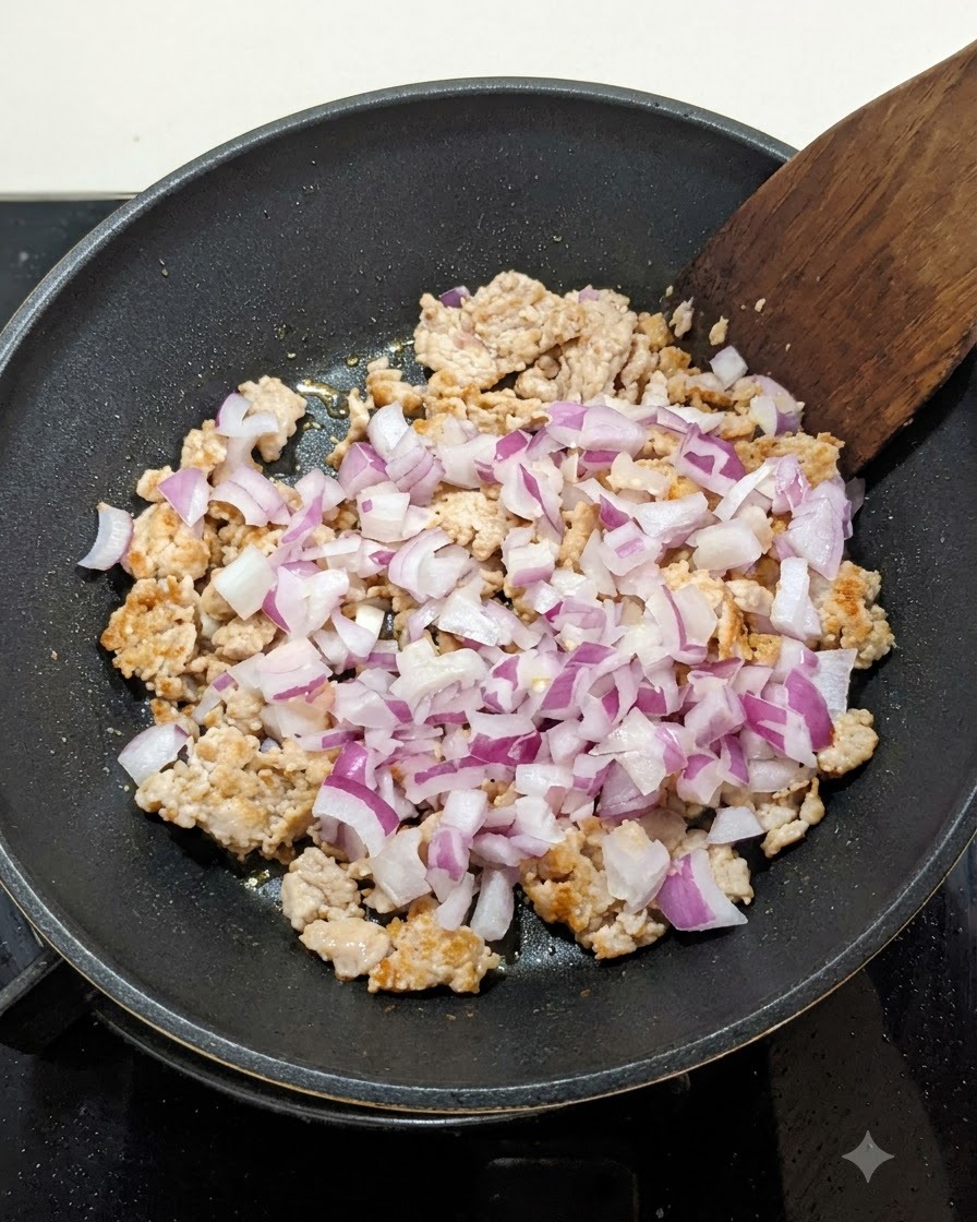 Cebolla roja picada mezclada con la carne dorada en una sartén, removida con una espátula de madera.