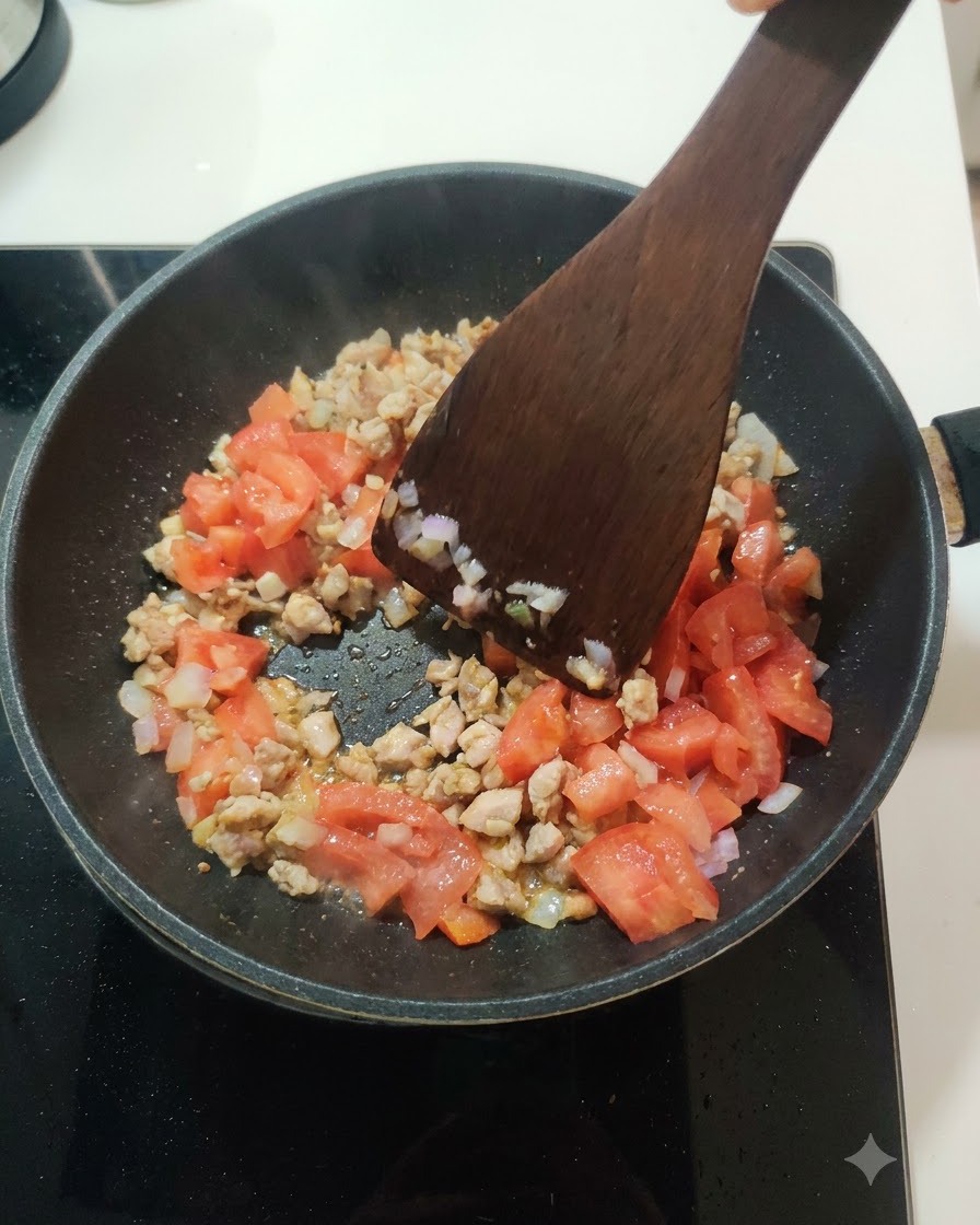 Tomates frescos picados integrándose con la mezcla de carne y cebolla dentro de una sartén.