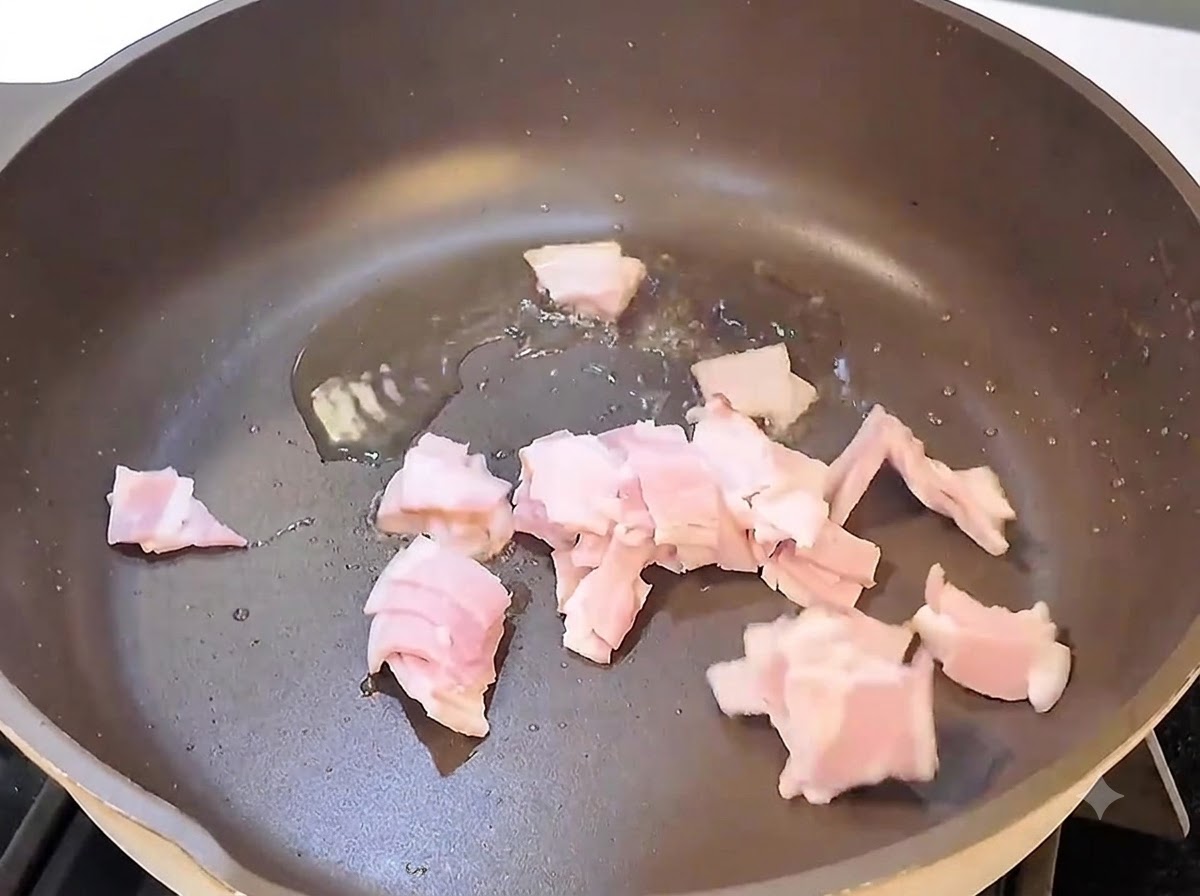 Trozos de tocino chisporroteando y friéndose en una sartén negra a fuego vivo.