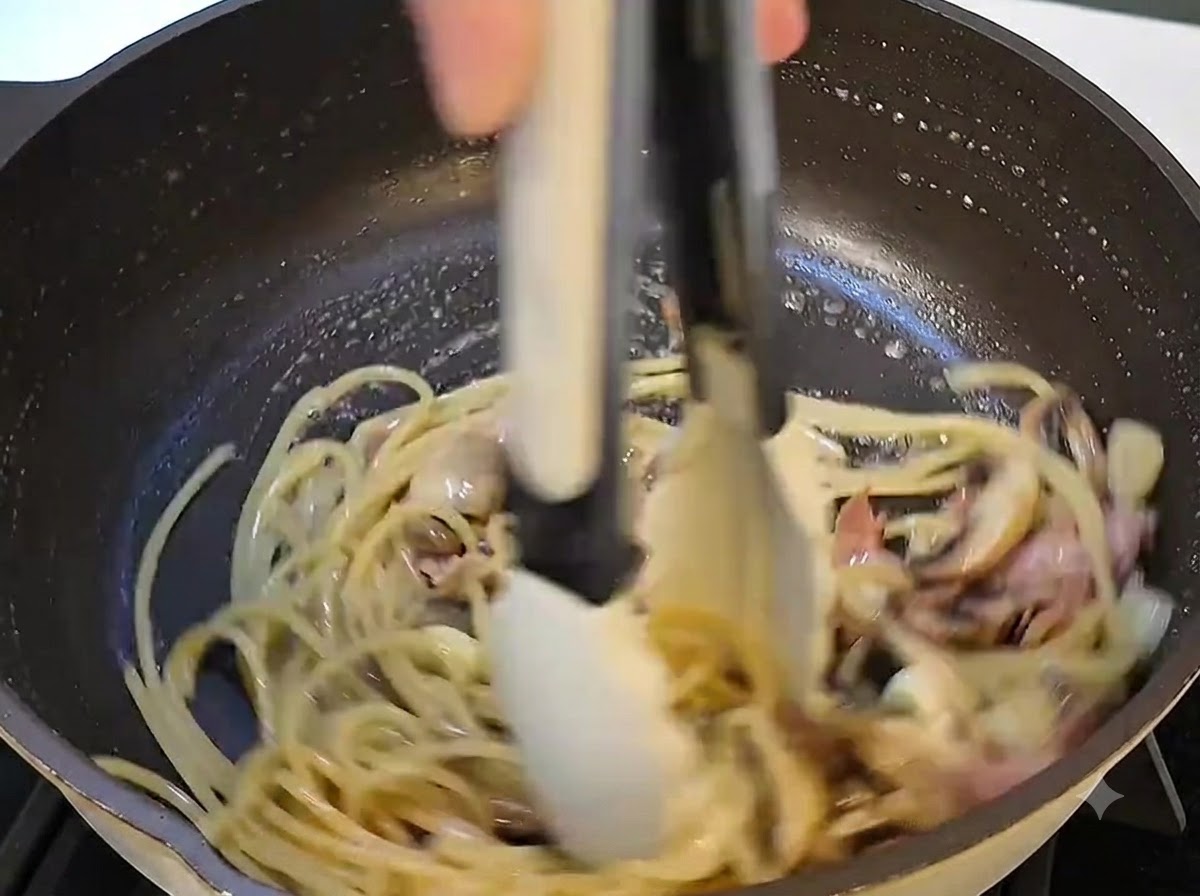 Una vista de cerca de la mantequilla siendo añadida y derritiéndose en la mezcla de pasta dentro de la sartén.