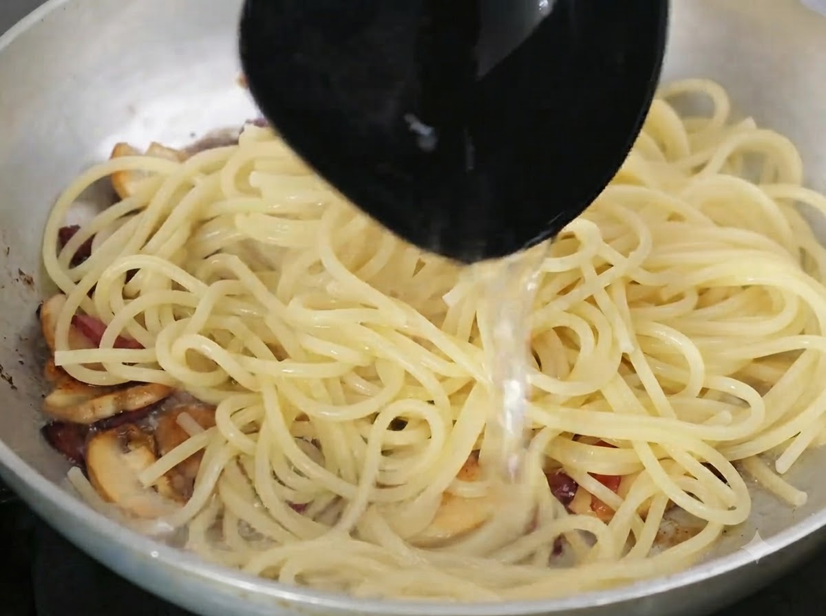 Un cucharón vertiendo agua rica en almidón en la sartén que contiene la pasta y los ingredientes.