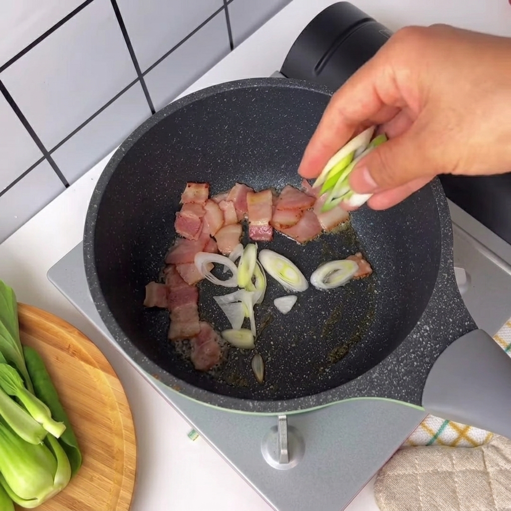 Cebolletas picadas y chile espolvoreados en una sartén con trozos de tocino crepitante.