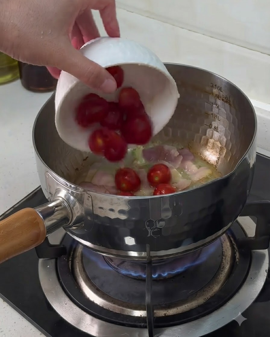 Tomates cherry agregándose desde un tazón blanco a una olla que contiene trozos de bacon cocinándose.