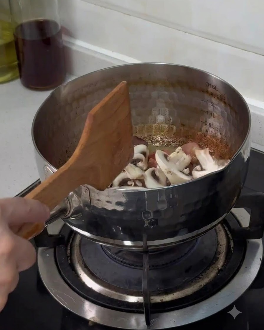 Champiñones botón frescos recién cortados cayendo en una olla de acero inoxidable y mezclándose con una espátula de madera.