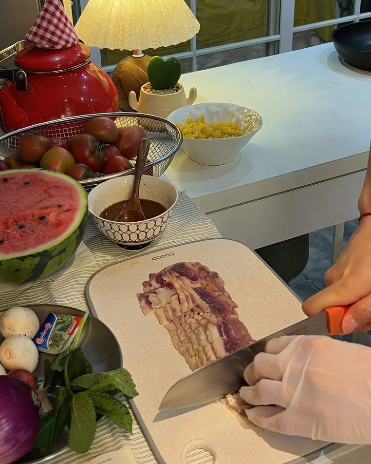 Una cebolla morada siendo cortada a la mitad en una tabla de cortar junto a un plato de champiñones y menta fresca.